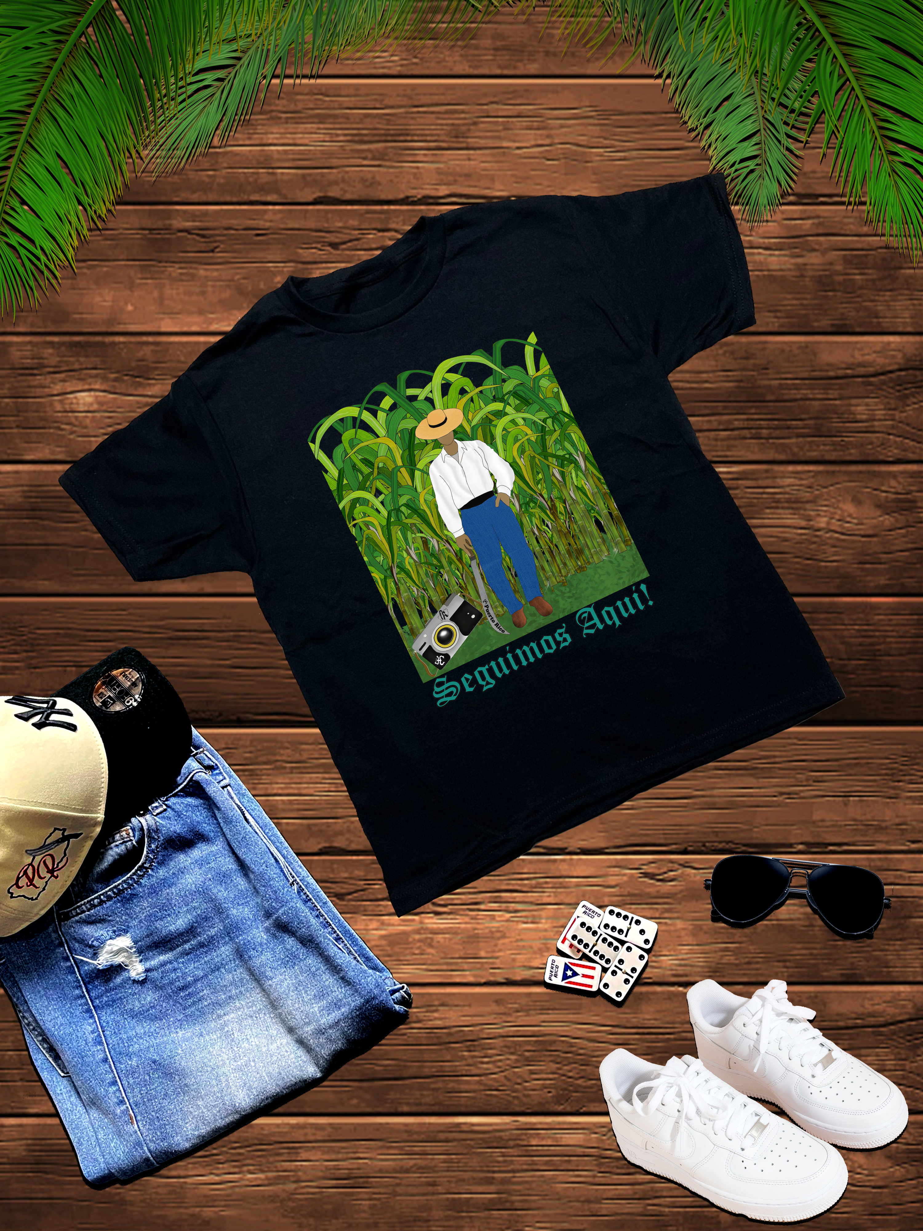 Black t-shirt with a graphic design on a wooden surface with jeans, sneakers, and sunglasses.